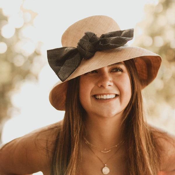 Woman wearing a wide-brimmed hat with a black bow outdoors