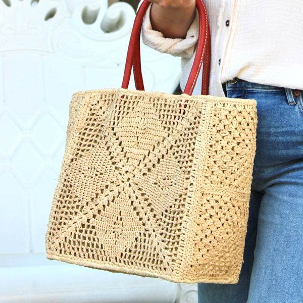 Person holding a woven bag with red handles against a blurred background