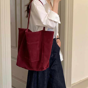 Person holding a red tote bag in a room with wooden flooring and white walls.