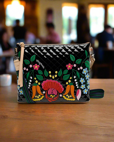 Black quilted handbag with colorful floral embroidery on a sunny background