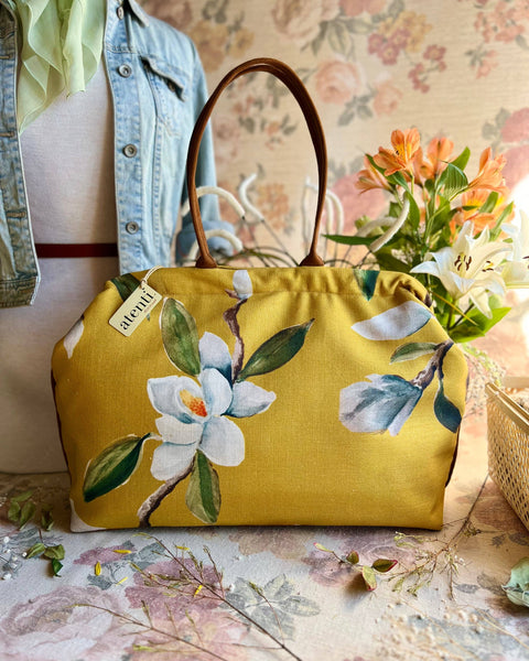 Yellow floral handbag on a white magnolia floral-patterned surface.
