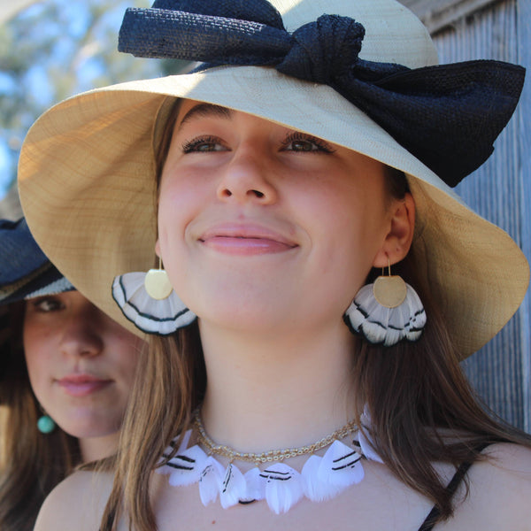 Woman wearing a large sun hat with a bow, standing outdoors.