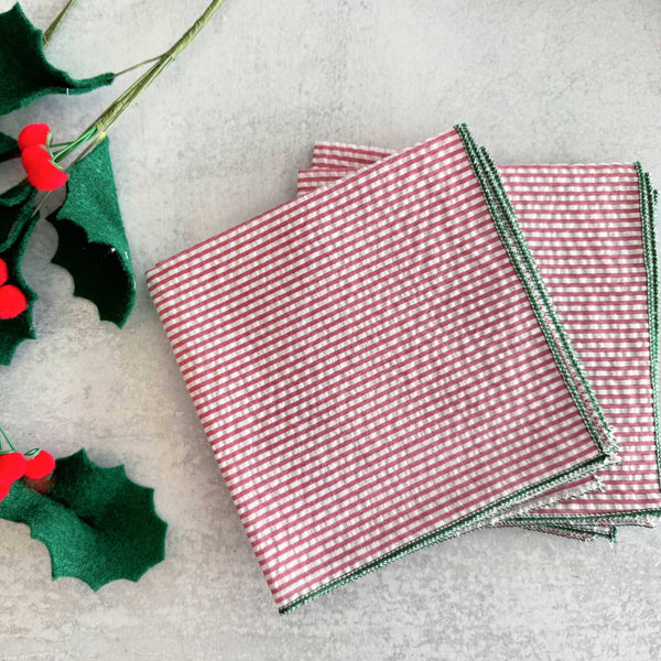 Red and white checkered napkins with green holly leaves on a light gray background