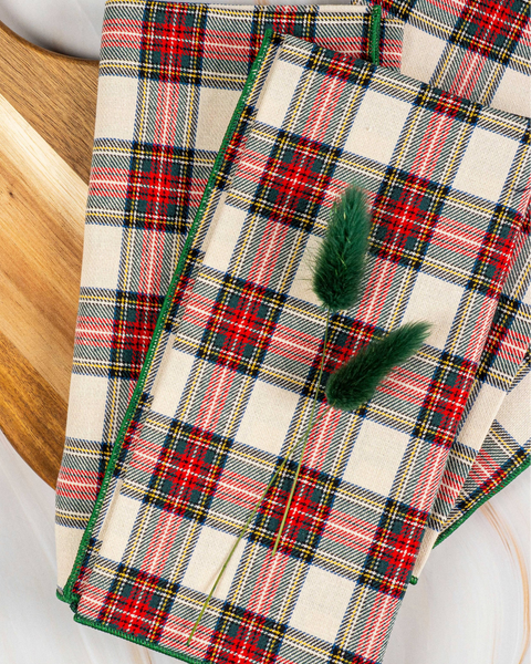 Plaid towel with green trim and a pine leaf on a wooden surface