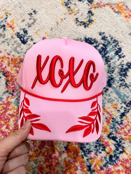 Pink cap with red 'XOXO' text held over a multicolored patterned surface