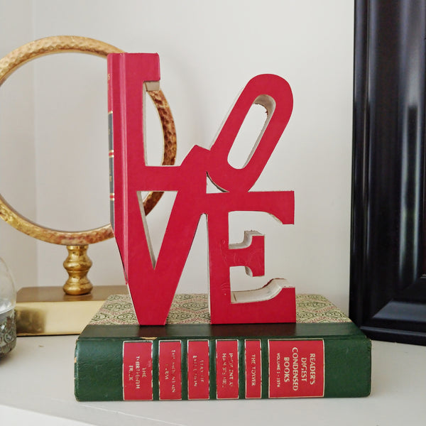 Vintage Red Book that has been cutout into the word LOVE sitting on a bookshelf as decor.